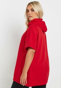 Röd överdimensionerad hoodie med huva och korta ärmar. Tillverkad av mjukt material, med en slät textur och en avslappnad passform.