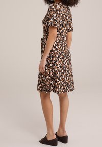 Robe à manches courtes brun, noir et blanc avec un motif, dotée d'une taille ceinturée et d'une jupe évasée, assortie avec des mules à talons bruns.