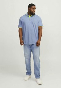 Modré polo tričko se zelenými akcenty, krátkými rukávy a límečkem, kombinované se světle modrými džínami a bílými teniskami. Jednoduchý, klasický design.