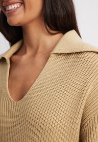 Maglione beige lavorato a maglia con scollo a V, colletto oversize e tessuto testurizzato con motivo a coste.