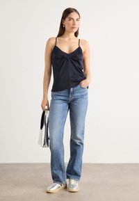 Marineblå satintopp med tynne stropper, drapert halslinning, kombinert med lyseblå jeans og sølvfargede sneakers; holder en metallisk veske.