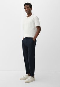 Korte mouwen witte t-shirt, marineblauwe elastische taillebroek en beige sneakers. Minimalistisch ontwerp met zakken en strakke lijnen.