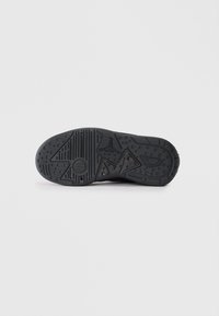 Suela de zapatilla negra con patrones texturizados, que incluyen elementos de tracción circulares y lineales, fabricada en goma para ofrecer agarre y durabilidad.