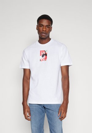 Hvid bomulds T-shirt med et centralt grafisk print i rød og sort. Klassisk rund hals og korte ærmer. Løs pasform.