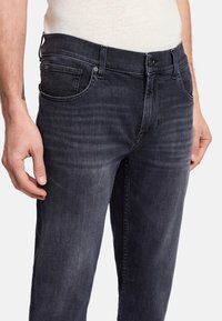 Mörkgrå denimjeans med en slät yta, standard femfickorsdesign och en knappstängning i midjan. Bleka områden på framsidan.