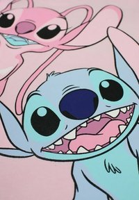 Personnages de dessin animé Stitch et Angel sur un fond rose pâle ; Stitch a une peau bleue, de grands yeux et des dents pointues ; Angel est rose avec de longues oreilles.