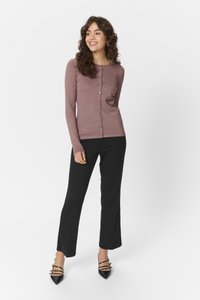 Lichtpaarse long-sleeve cardigan gemaakt van rib materiaal, met een knoopsluiting aan de voorkant en een getailleerd ontwerp. Gepaard met zwarte broeken en puntige schoenen.