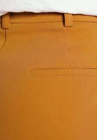 Senapsgula tygbyxor med en slät textur, prydda med en platt bakficka och en diskret lyster. Enkel design med bältesöglor.