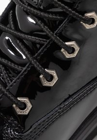 Stivale in pelle verniciata nera con hardware esagonale in argento, dotato di lacci neri intrecciati e cuciture dettagliate lungo la suola.
