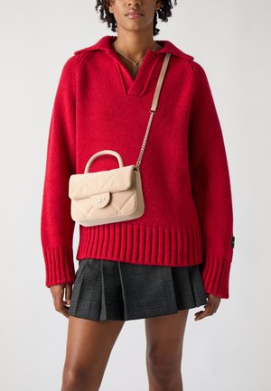 Maglione rosso a maglia con scollatura a V e orlo a costine, abbinato a una gonna pieghettata a quadri nera. Una piccola borsa a tracolla beige trapuntata con manico superiore pende da una catena.