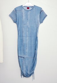 Robe midi patchwork en jean à manches courtes avec détail lien coulissant à l'ourlet, suspendue sur un cintre blanc contre un mur uni.