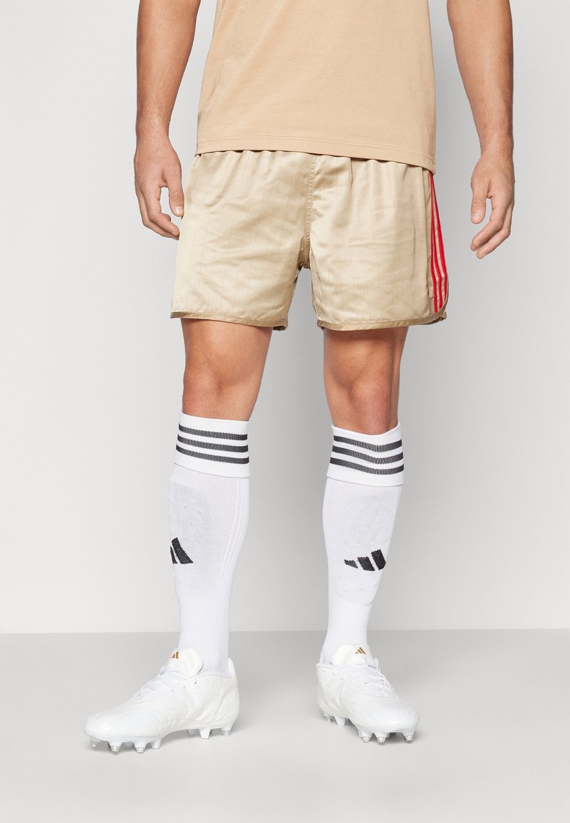 Beiga fotbollsshorts med vertikala ränder, röda sidokanter, tillsammans med vita knästrumpor med svarta ränder och vita fotbollsskor.