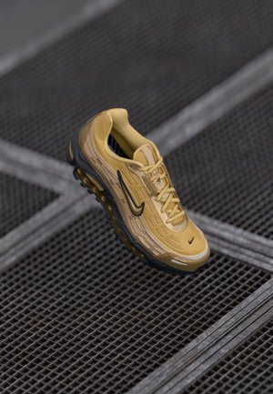 Chaussure de course Nike jaune et noire avec des lacets sur un sol en grille métallique.