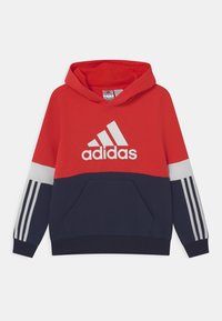 Červená a námořnická modrá mikina s kapucí, bílým logem Adidas, přední kapsou a třemi bílými pruhy na každém rukávu. Měkká látka, ležérní design.