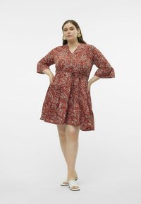 Robe rouge avec un motif paisley, décolleté en V, manches trois quarts et taille cintrée, évasant en une jupe jusqu'aux genoux.