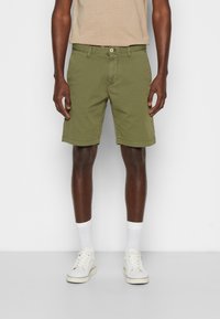 Olivgröna bomullsshorts med rak passform, sidofickor och knäppning, kombinerade med vita strumpor och sneakers.