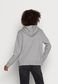 Szara bluza z kapturem o miękkiej fakturze, wyposażona w kieszeń kangurkę oraz prążkowane mankiety i dół. Na tyle znajduje się wzór przedstawiający kaptur i rękawy.