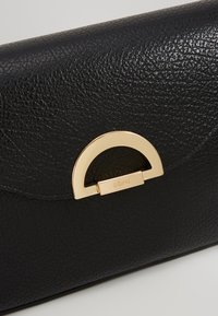 Pochette in pelle nera con finitura testurizzata, caratterizzata da una chiusura a mezzaluna dorata e un logo del marchio in rilievo sulla chiusura.