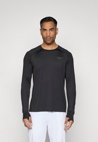 Ilga lieso juoda sportinė marškinė su apvalia apykakle, nykščio angomis ir mažas logotipas ant krūtinės. Minkšta, tampri medžiaga.