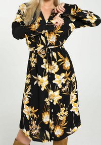 Robe noire à fleurs avec des fleurs jaunes et blanches, manches longues, devant à boutons et une ceinture à la taille. Tissu doux avec un design fluide.