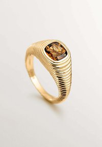 Anillo de oro con una piedra marrón de corte cuadrado. La banda presenta un diseño texturizado y estriado, con una superficie lisa alrededor de la piedra.