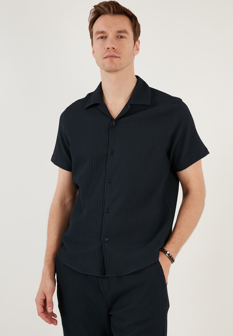 Zwarte kortekolen shirt met een kraag, met een geribbelde textuur en een knoopsluiting. Gecombineerd met bijpassende broek voor een samenhangende uitstraling.