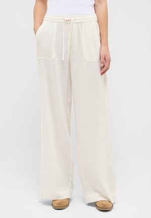 Løse hvide hørbukser med snøre i taljen og forlommer, båret med brune sko og hvid top.