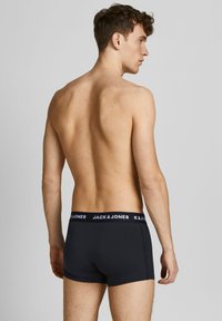 Schwarze Boxer-Shorts mit einem kontrastierenden weißen Bund, auf dem der Markenname "JACK & JONES" steht. Glatter Stoff, enganliegendes Design, mittelhoher Schnitt.