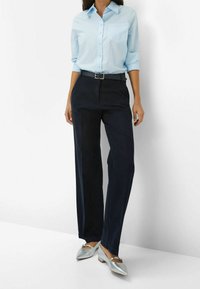 Chemise bleu clair à boutons, pantalons larges navy, ceinture noire et ballerines argentées à talons pointus avec un accent en nœud. Tissu lisse et coupe ajustée.
