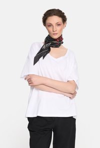 Biała koszulka z krótkim rękawem, luźny krój i dekolt w serek. Połączona z czarnym wzorzystym szalem związanym na szyi. Gładkie czarne spodnie.