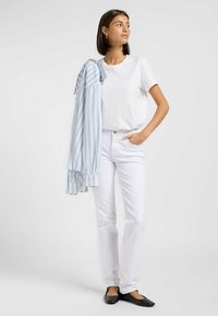 Camiseta de algodón blanca, camisa a rayas azul clara colgada del brazo, pantalones de mezclilla blancos y bailarinas negras. Diseño simple y limpio.