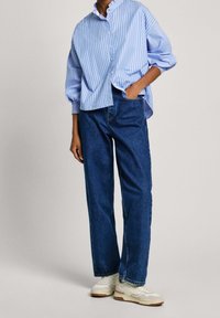 Randig blå skjorta med puffärmar, kombinerad med raka mörkblå jeans och vita sneakers med beige sula.