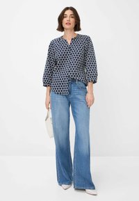 Navybluse mit weißem kreisförmigem Muster, drei Viertelärmeln und einem V-Ausschnitt. Kombiniert mit hellblauen Schlagjeans und einer kleinen weißen Tasche.