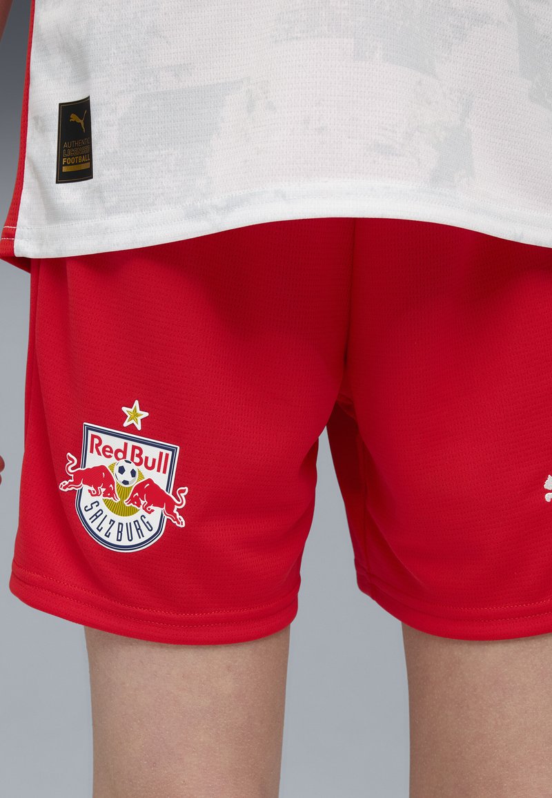 Röda fotbollsshorts i ventilerande tyg, med Red Bull Salzburgs logotyp och detaljerad brodyr. Klara röda färg med en slät textur.