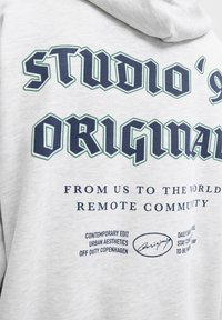 Sudadera gris con el texto en negrita "STUDIO' 90 ORIGINAL" en navy, con texto adicional más pequeño abajo. Tejido suave, diseño casual y corte relajado.