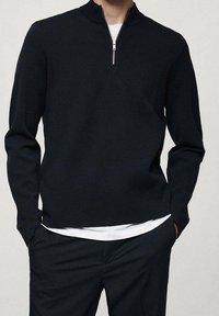 Pull-over noir avec un col à demi-fermeture éclair, fabriqué en maille douce, avec des manches longues et une coupe décontractée.