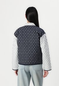Quilted jacket with navy and white patterned fabric, featuring a collared neck and contrasting textures on sleeves. Classic fit and casual style.