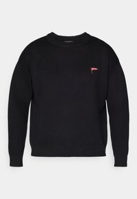 Svart strikket genser med rund hals, ribbestrikkede mansjetter og kant, med en liten rød logo på forsiden. Koselig og uformell design.