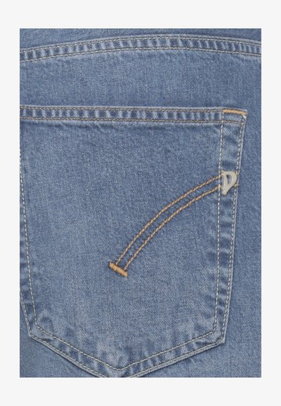 Poche arrière d'un jean en denim bleu avec une double couture orange et un petit logo métallique sur le côté droit de la poche.