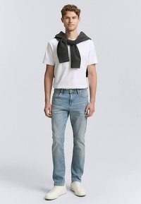 Biała koszulka z okrągłym dekoltem, na ramionach przewieszony ciemnoszary sweter, jasnoniebieskie dżinsy i białe trampki.