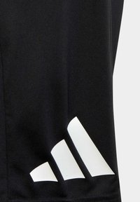 Camisa atlética negra con un gran logo blanco de Adidas en la parte inferior izquierda, hecha de un tejido suave y ligero con un diseño ajustado.