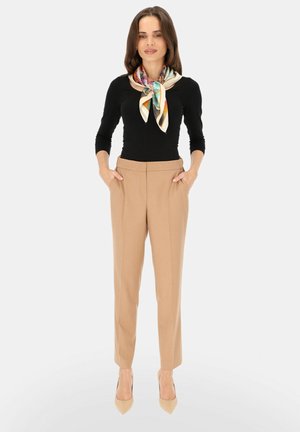 Beżowe, dopasowane spodnie o prostym kroju, w połączeniu z czarną bluzką z długim rękawem i kolorowym, wzorzystym szalikiem na szyi.