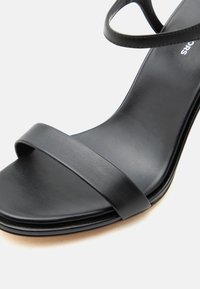 Μαύρο σανδάλι με ανοιχτά δάχτυλα, με έναν μπροστινό ιμάντα και έναν ιμάντα αστραγάλου, με λείο τελείωμα από συνθετικό δέρμα.