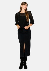 Pullover nero lavorato a maglia con un design testurizzato e maniche a tre quarti, abbinato a una gonna di jeans nera con uno spacco frontale. Stivali neri fino al ginocchio.