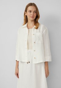 Witte cropped jas van textiel, met een kraag, knoopsluiting en een borstzak. Gedragen over een bijpassend licht topje.
