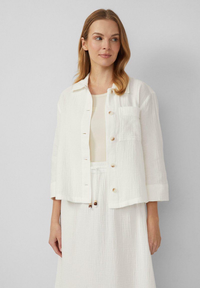 Witte cropped jas van textiel, met een kraag, knoopsluiting en een borstzak. Gedragen over een bijpassend licht topje.
