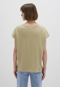 Olive green short-sleeve T-shirt, relaxed fit, round neckline, textured fabric, slightly longer back hem, worn with light blue jeans.