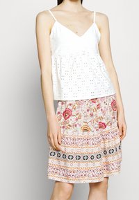 Žena v bílém bezramíčkovém topu s výšivkou a růžové květinové sukni s černými a žlutými proužkovými vzory.