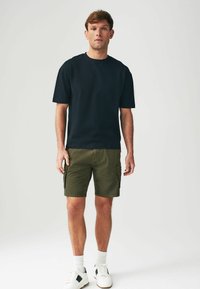 Tricou negru cu mânecă scurtă, asortat cu pantaloni scurți cargo de culoare verde măsliniu. Adidași cu bază albă și accente negre. Design simplu, casual.