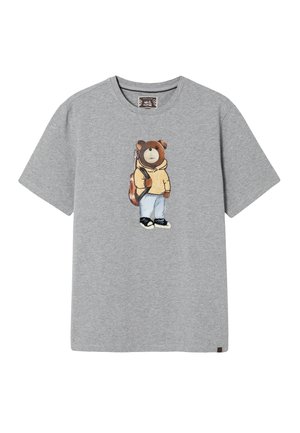 Siva bombažna majica z grafiko medvedka v rumeni kapucarji in modrih kavbojkah, s črnimi čevlji in nahrbtnikom. Kratki rokavi, zaobljen vratni izrez.